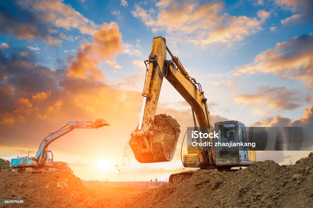 excavator in construction site on sunset sky excavator in construction site on sunset sky background Backhoe Stock Photo