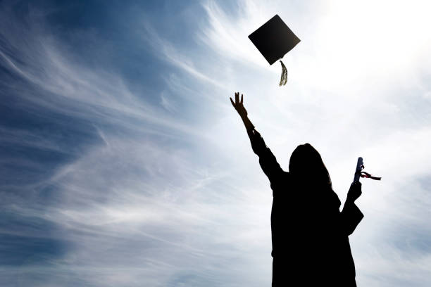 istock Graduate students tossing up hats over blue sky 664980354