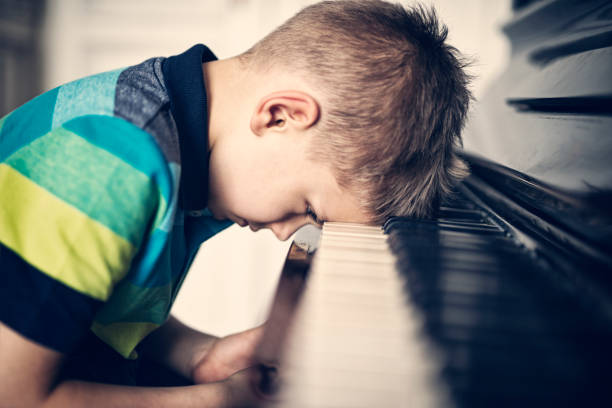 depressed little boy frustrated with his piano lesson - practicing piano child playing imagens e fotografias de stock