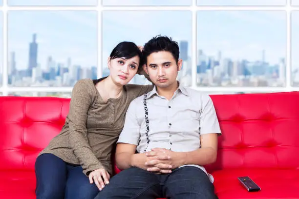 Bored young couple watching television at apartment with cityscape background