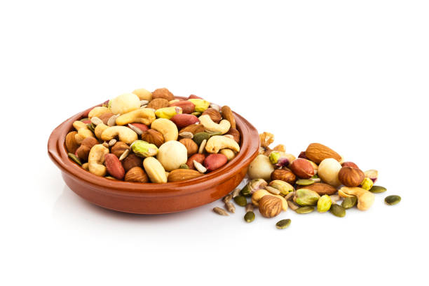 Horizontal shot of a brown bowl filled with mixed nuts isolated on white background. Some nuts are spilled beside the bowl. Nuts included in the composition are pistachios, hazelnut, pine nut, almonds, pumpkin seeds, macadamia nuts, sunflower seeds, peanuts, cashew and walnuts. DSRL studio photo taken with Canon EOS 5D Mk II and Canon EF 100mm f/2.8L Macro IS USM