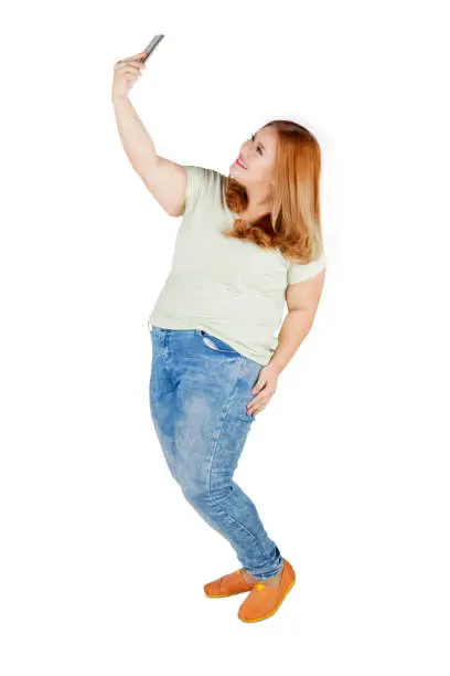Full length of blonde woman with overweight body, taking selfie photo with her mobile phone in the studio