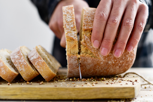 closeup of a young caucasian man cutting a loaf of bread in slices with a knife