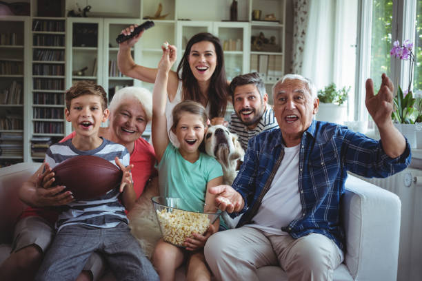 feliz múltiples generaciones familiares viendo partido de fútbol en la televisión en la sala de estar - retirement grandfather senior adult child fotografías e imágenes de stock