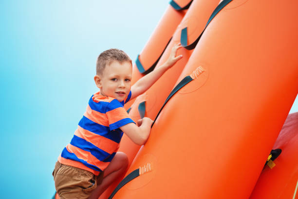 маленький мальчик, играющий на надувной детской площадке на пляже - child balloon outdoors little boys стоковые фото и изображения