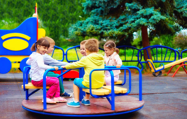 group of happy kids having fun on roundabout at playground group of happy kids having fun on roundabout at playground swing play equipment stock pictures, royalty-free photos & images