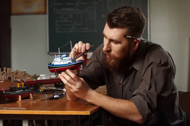 Young man constructing a ship model in a ship-modelling studio. He is wearing a checkered shirt.