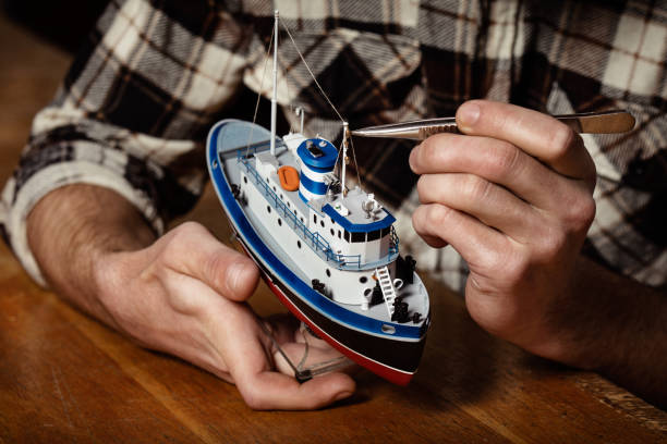 Young man constructing a ship model Young man constructing a ship model in a ship-modelling studio. He is wearing a checkered shirt. toy boat stock pictures, royalty-free photos & images