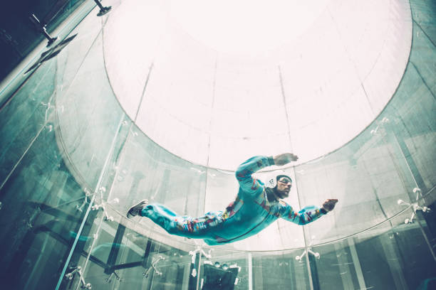 Indoors skydiving - one young man practising freefall simulation View through window - glass reflections. Indoor skydiving is the simulation of true freefall conditions in a vertical wind tunnel, Logatec, Slovenia, Europe. Copy space, No logo. Lens 24.0-70.0 mm f/2.8 skydiving stock pictures, royalty-free photos & images