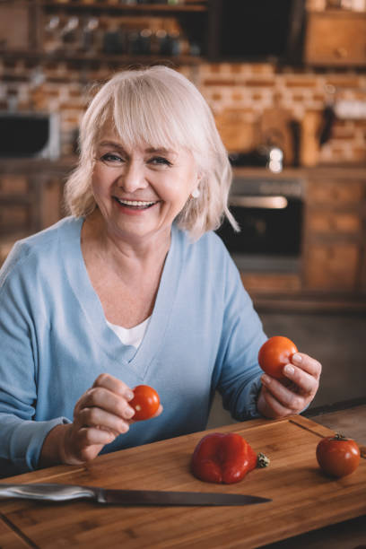 istock Happy senior woman holding tomatoes while cooking at kitchen 665040138