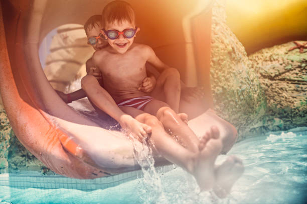 Kids playing in resort pool slide. Kids aged 6 are wearing swimming goggles and are sliding down to the pool.\n