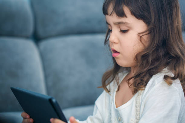 istock Cute little girl sitting on sofa with tablet in her hands 665055452