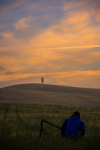 Rear view of man photographing fields and hill in Tuscany. Tranquil view of agricultural land against sky during sunset. Beautiful view of nature in Italy.