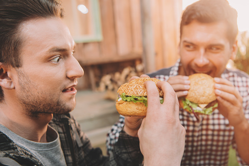 Emotional young men eating gourmet hamburgers outdoors