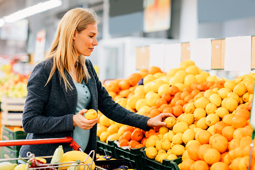 Pregnant Woman Shopping in Supermarket. Choosing fruits and putting in shopping chart