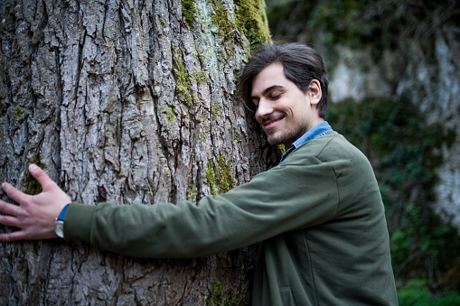 Young man hugging an old tree in the forest