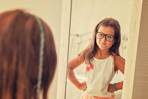 LIttle girl in glasses looking in the mirror.