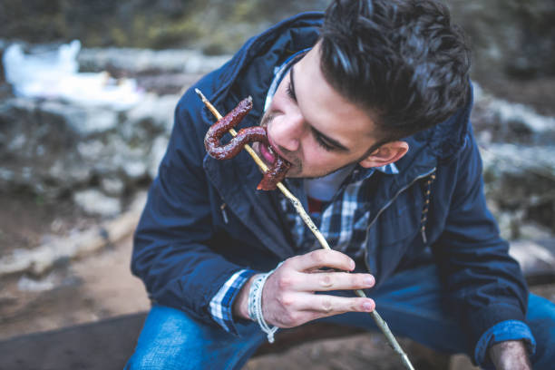 Young man eating hot dog on a stick in the nature