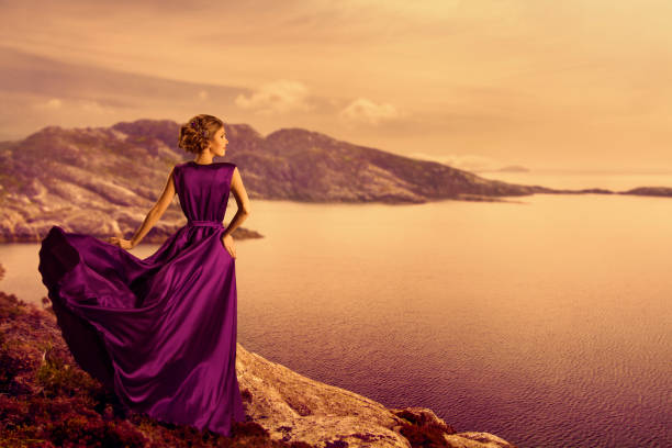 マウンテンコーストのエレガントなドレスを着た女性、流れるガウンのファッションモデル、目をそらす - mountain looking at view beach cliff ストックフォトと画像