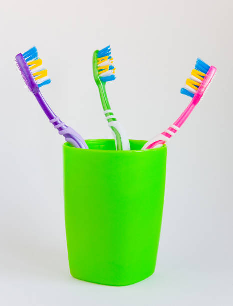 istock Hygiene. Three beautiful multi-colored toothbrushes stand in a green glass on a light background. 665104180