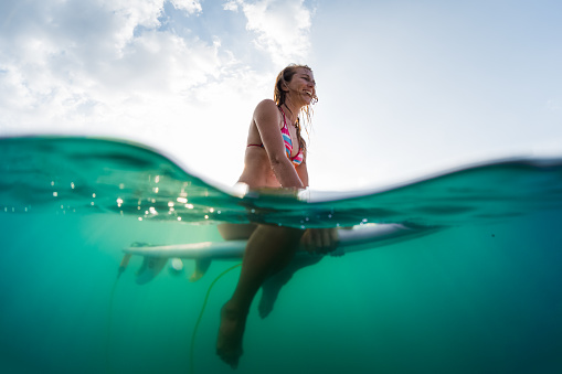 Splitted shot with underwater view of the happy woman sitting on the surfboard in the ocean