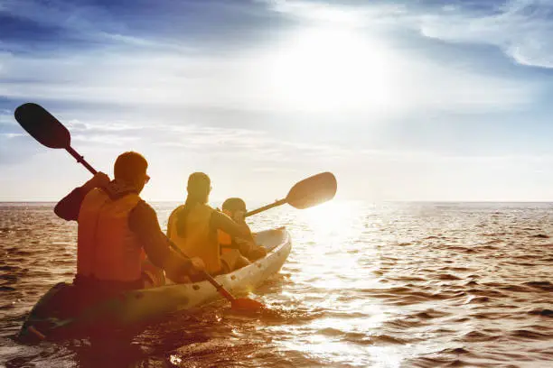 Kayaking concept with family of father mother and son swimming at sea at sunset time. Space for text