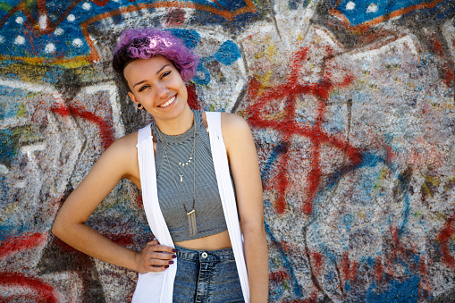 Smiling young hipster girl posing against graffiti wall