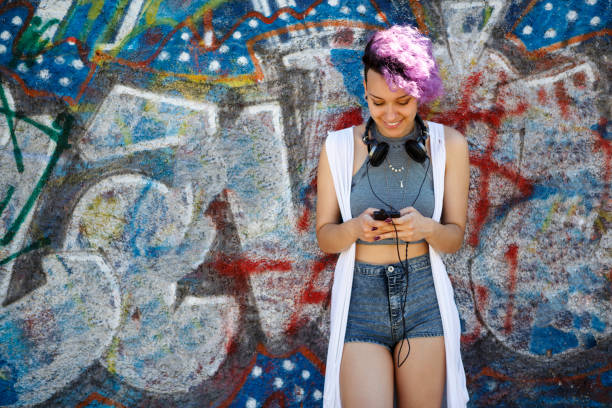 istock Smiling young hipster girl using smart phone against graffiti wall 665132682