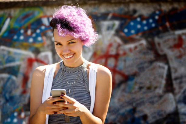 istock Smiling young hipster girl using smart phone against graffiti wall 665134842
