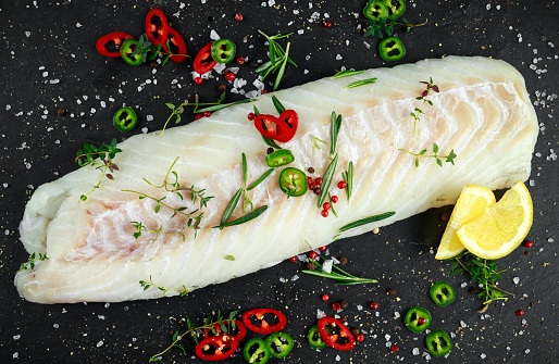 Fresh Raw Cod loin fillet with rosemary, chillies, cracked pepper and lemon on stone board.