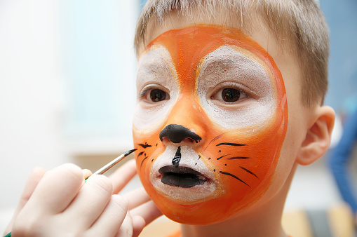 Make up artist making tiger mask for child.Children face painting. Boy  painted as tiger or ferocious lion. Preparing for theatrical performance. Boy actor playing role. Tiger mask face