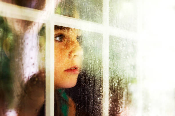 istock Little girl looking out window that has been wet with rain. 665165976