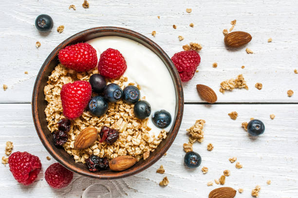 bowl of oat granola with yogurt, fresh raspberries, blueberries bowl of oat granola with yogurt, fresh raspberries, blueberries and nuts on white wooden board for healthy breakfast. top view bowl stock pictures, royalty-free photos & images