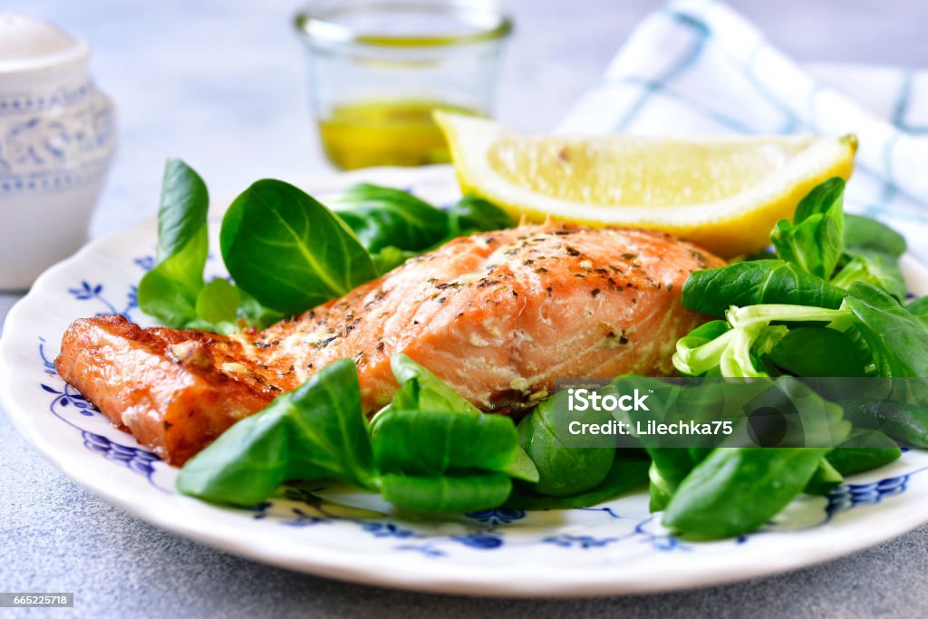 Grilled organic salmon with salad leaves on a vintage plate Grilled organic salmon with salad leaves on a vintage plate on light slate,stone or concrete background. Salad Stock Photo