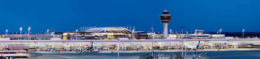 Franz-Josef-Strauss Munich airport with control tower, three passenger airplanes standing at the gates, apron area, long exposure with tripod, horizontally stitched composition.