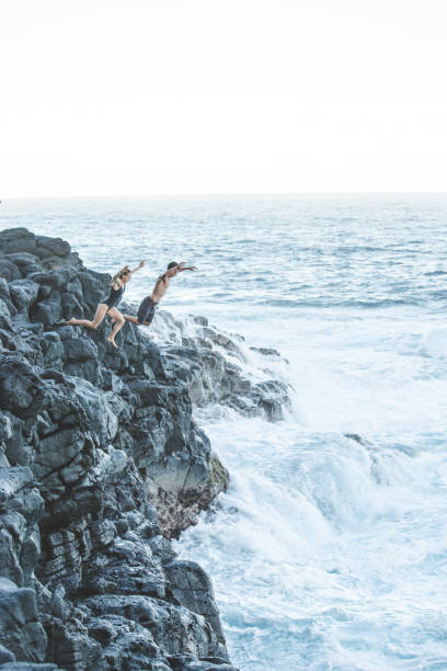 istock Beautiful couple jumping off cliff into ocean 665225958