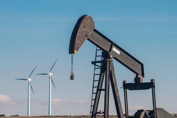 pompa dell'olio e mulini a vento - oil pump oil industry prairie field foto e immagini stock