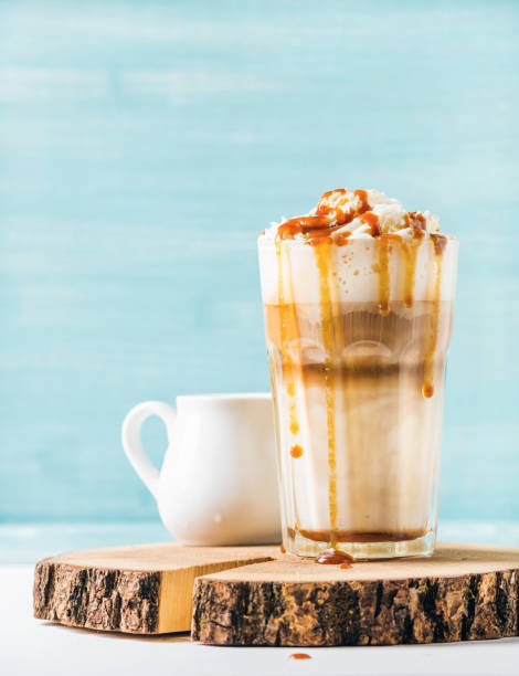 latte macchiato with whipped cream and caramel sauce in tall glass on wooden board over blue painted wall background, copy space - caramel latté coffee cafe macchiato imagens e fotografias de stock