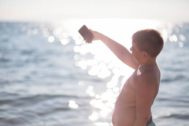 boy on the beach making selfie boy on the beach making selfie overweight boy stock pictures, royalty-free photos & images