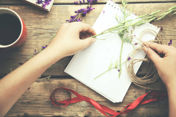 istock woman hand ribbon, flower, notebook and coffee on table 665252416