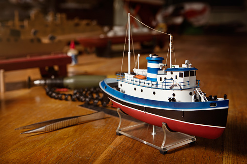 Ship model stands on the table. The ship is painted in red, white, blue, black. Near the ship model on the table laid some instruments.
