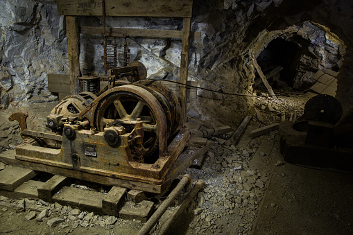 An old hoist and several other pieces of worn-down mining equipment inside of an abandonned mine in Western Utah. The hoist would have been used to pull loaded mine carts up a nearby steep sloping shaft before they were pushed out of the mine to process the ore.