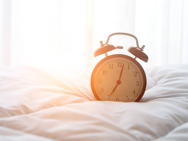 istock Alarm clock on bed in morning with sun light 665280932