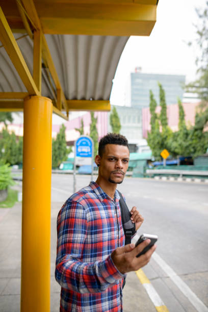 istock Young handsome African man holding mobile phone while waiting for the bus at bus stop 665281000