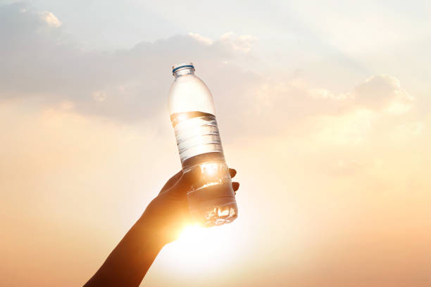 mano che tiene l'acqua potabile sullo sfondo del tramonto - water bottle water bottle drinking foto e immagini stock