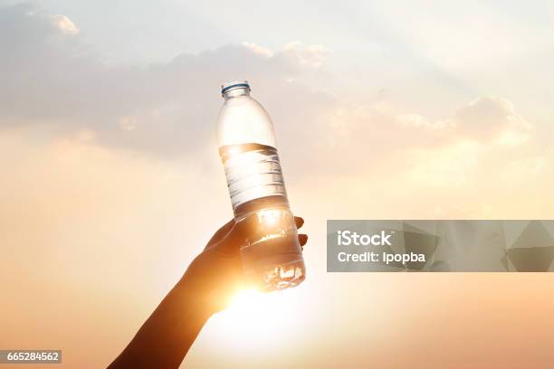 Hand Holding Drinking Water On Sunset Background Stock Photo - Download Image Now - Drinking, Water, Water Bottle