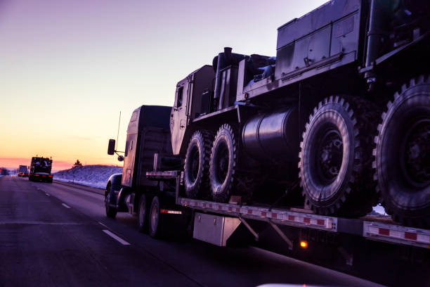 Expressway Flatbed Semi Truck Convoy Hauling Armored Military Land Vehicles Heading west into a dusky winter sunset, a convoy of semi tractor trailer flatbed trucks loaded with heavy, oversized United States Army tactical armored military land vehicles is hauling the freight along a remote stretch of expressway through the western USA state of Utah. NOTE: Vehicle details have been altered - with various subtractions and/or additions - to make them generic. armoured truck stock pictures, royalty-free photos & images