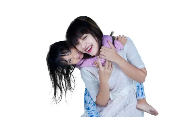 Cheerful young mother and her daughter doing piggyback ride in the studio, isolated on white background