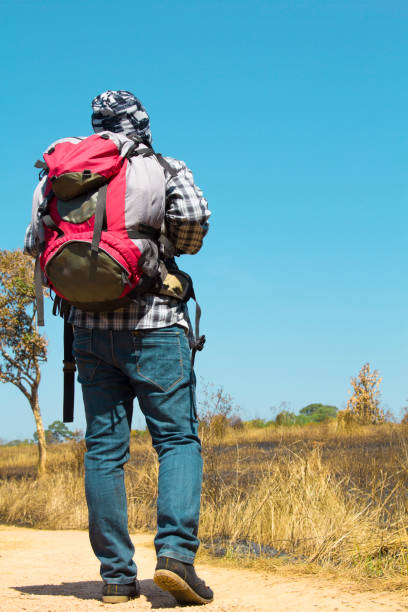 istock Backpacker wearing a red large backpack of camping gear walking through hilly scrub standing facing away from the Camera 665305330