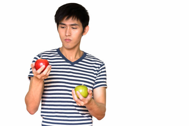 istock Studio shot of young handsome Asian man holding green apple and red apple while thinking against white background 665308966